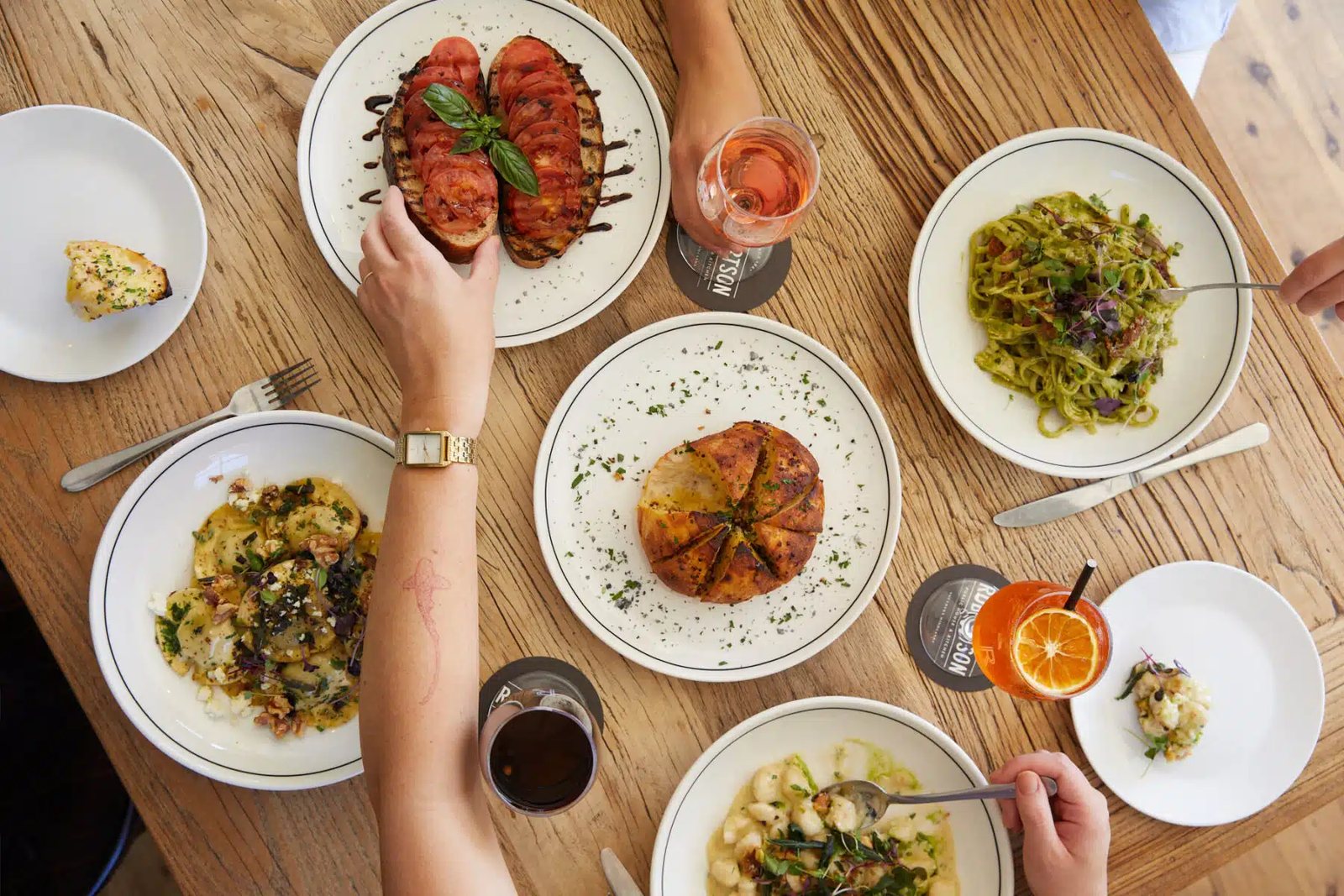 Plates of food on a timber table, hands reaching in