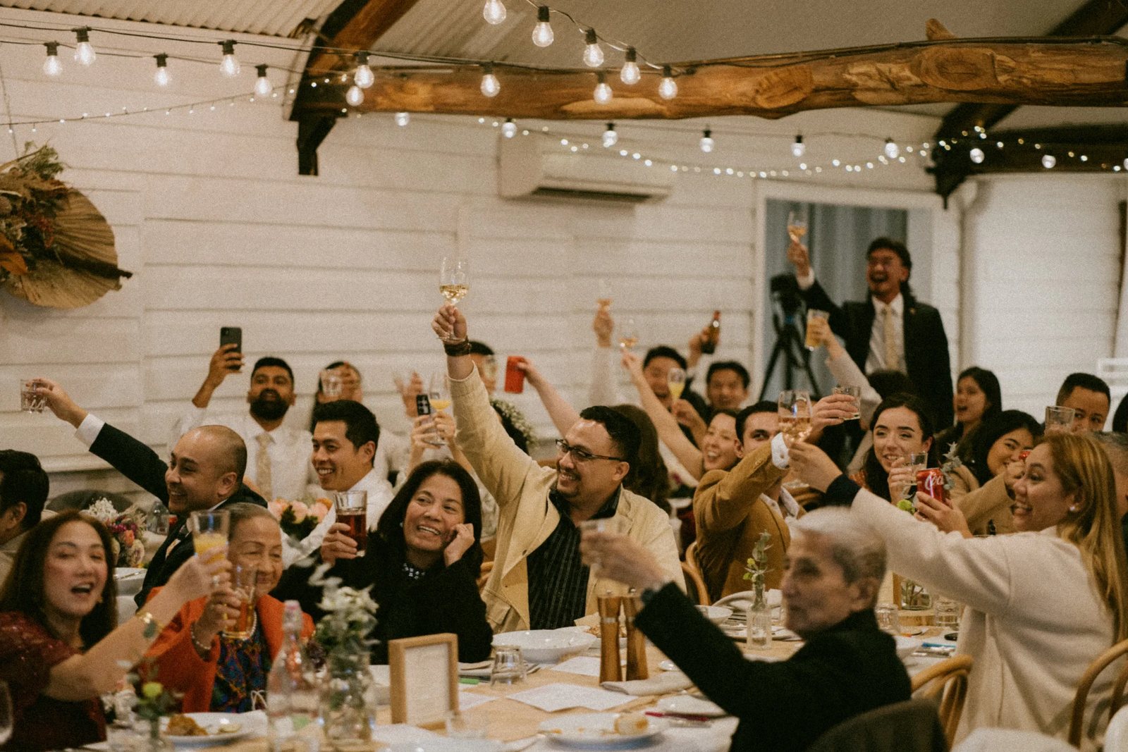 Guests on their feet cheering under the beams, glasses up
