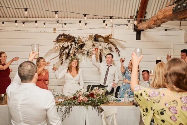 A couple toasting at the head table under a dried floral installation