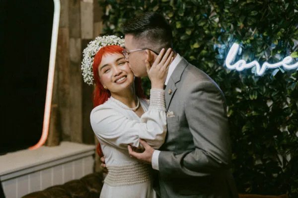A couple kissing in front of a neon love sign